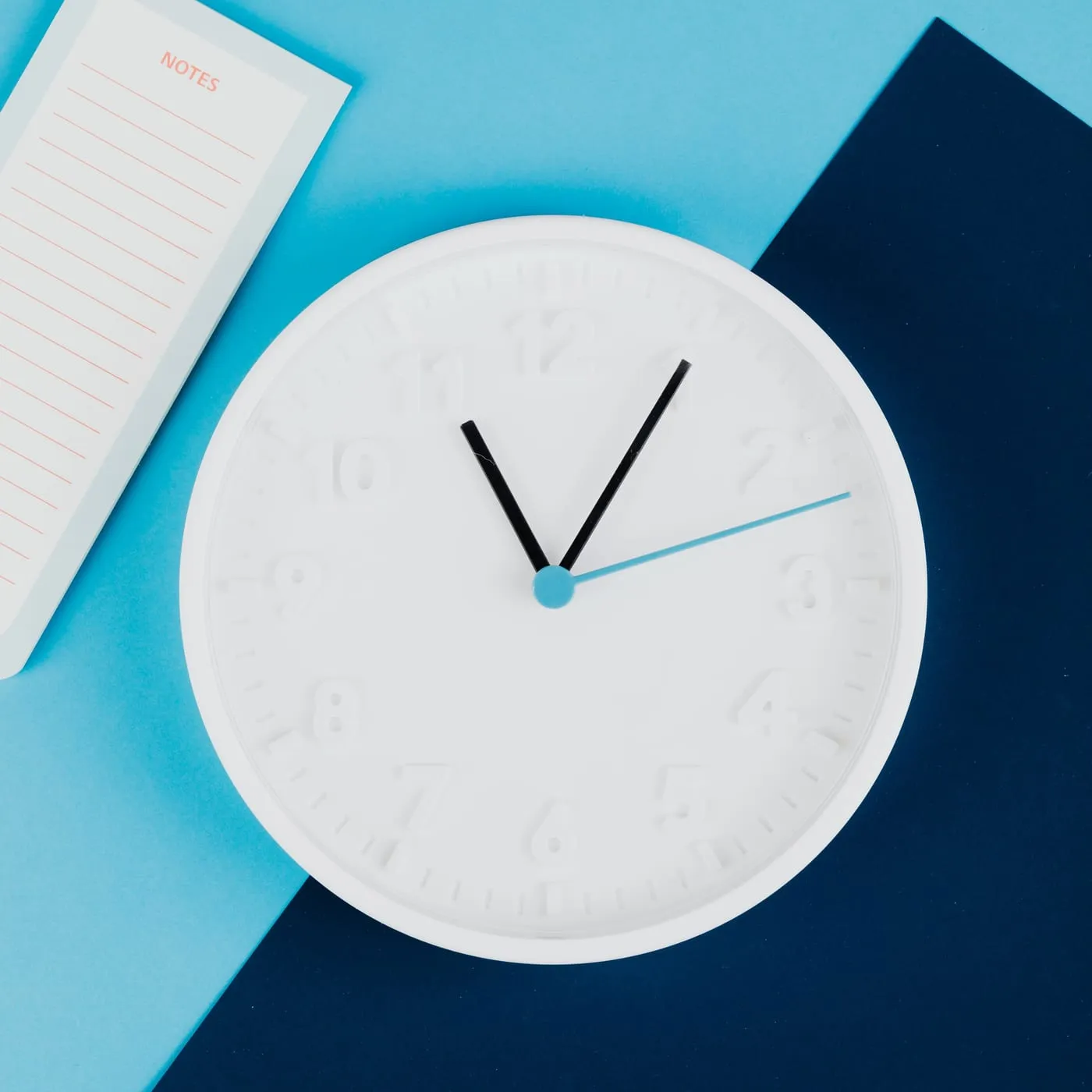 A white wall clock and a notepad on a blue and navy background